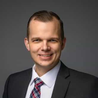 Professional headshot of Troy Anderson in a suit and tie, smiling confidently.