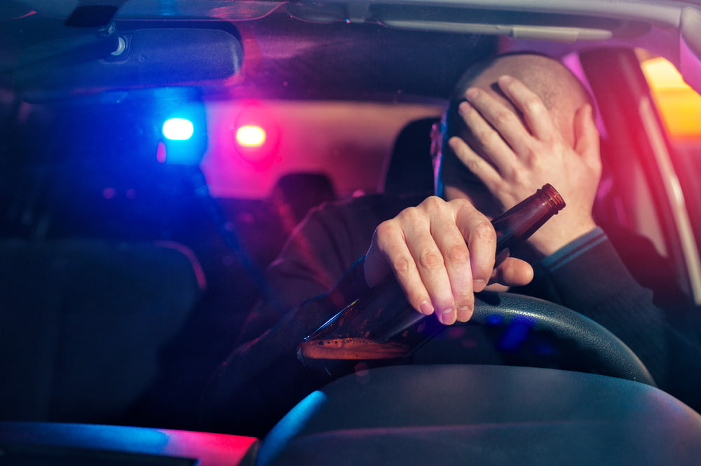 Man holds a beer while being detained by a police officer