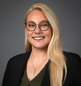 Professional headshot of Cara Maniscalco, a woman with long blonde hair and glasses, wearing a black blazer.