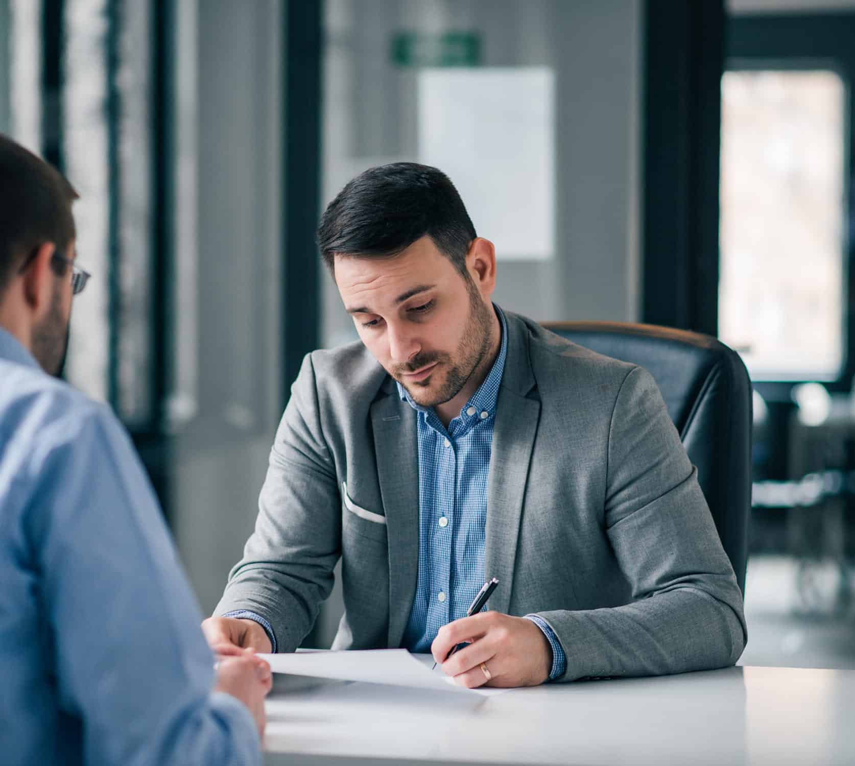Two professionals engaged in a business meeting, one reviewing documents while the other listens attentively.